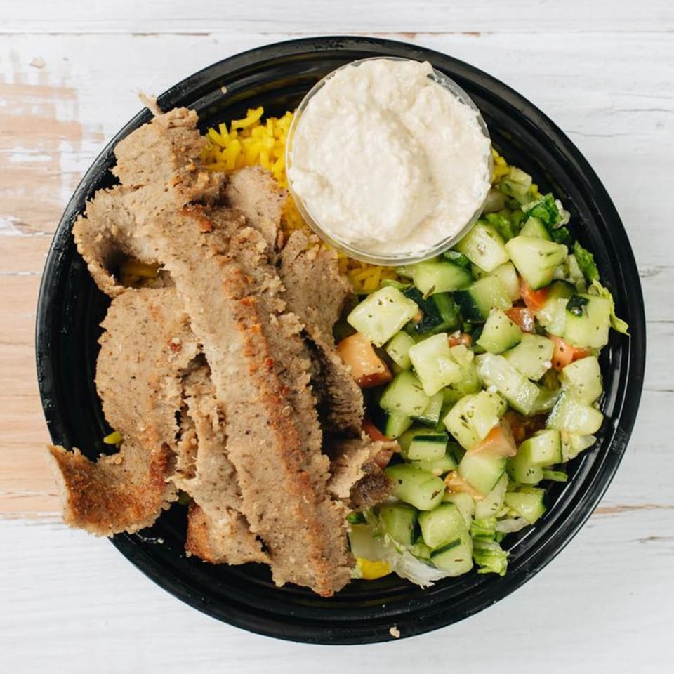 Overhead view of a black bowl with sliced gyro meat, yellow rice, cucumber salad, and hummus.