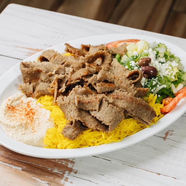 Gyro meat platter with yellow rice, hummus, and a Greek salad with feta and olives.
